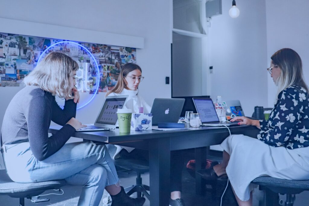 Três mulheres sentadas em uma mesa de trabalho usando os Canais de publicação de contatos inteligentes