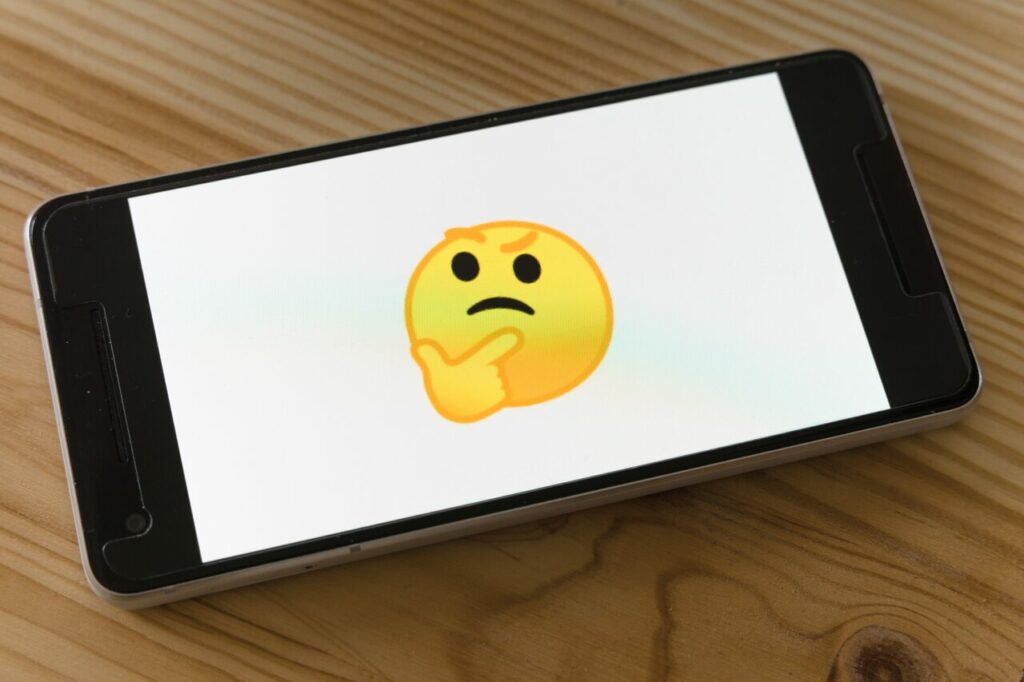 A imagem traz a foto de um celular com um emoji de rosto pensativo ao centro, na or amarela